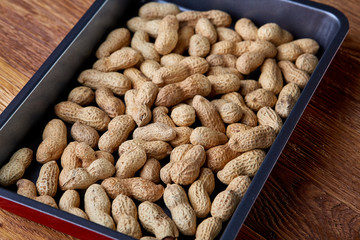 Unpeeled raw peanut on baking tray over wooden background, selective focus, shallow depth of field.