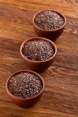 Three ceramic bowls with flaxseeds arrenged in row over wooden background, top view, selective focus