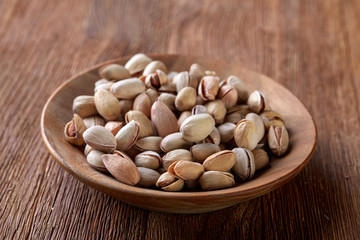 Salted pistachios on a wooden plate over wooden background, top view, close-up, selective focus.