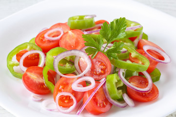 Healthy, fresh and delicious vegetable salad with cherry tomatoes, red onion rings, green pepper rings, parsley and olive oil