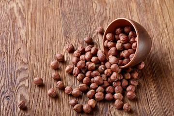 Hazelnuts in overturned ceramic bowl on wooden background with copy space, top view, selective focus.