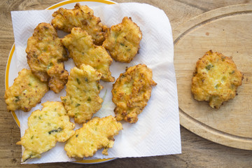 single corn fritter near a dish full of the same fritters