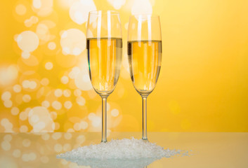 Two wonderful wineglass of champagne with bubbles of air, near handful of artificial snow on bright yellow