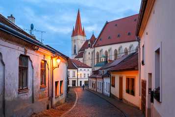 Obraz premium Old charming paved street with night illumination in the historical centre leading to the ancient St. Nicholas Church. Town of Znojmo, Czech Republic, South Moravia, Europe