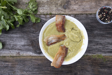 Pea puree with bacon in a white plate on a wooden background.