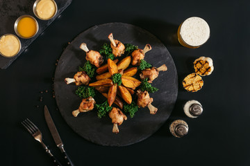 top view of baked potatoes with chicken, glass of beer, grilled garlic and spices on black