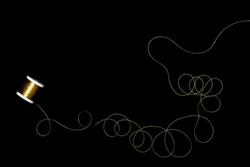 Spool of gold thread on a black background.	