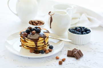Traditional breakfast concept. Stack of pancakes with chocolate sauce, blueberries and nuts on white table cloth. Selective focus
