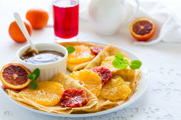 French pancakes. Crepe Suzette with caramel, oranges, blueberries, almonds and hazelnuts on white table cloth