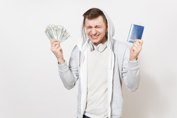 Young overjoyed excited man in t-shirt, light sweatshirt with hood with headphones holds international passport, bundle of dollars, cash money isolated on white background. Concept of travel, tourism.