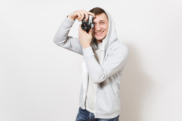 Young handsome smiling man student in t-shirt and light sweatshirt with hood with headphones takes pictures on retro camera isolated on white background. Concept of photography, hobby