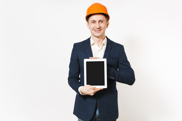 Young handsome smiling businessman in dark suit, protective hardhat holding tablet pc computer with blank screen isolated on white background. Male worker for advertisement. Business, working concept.