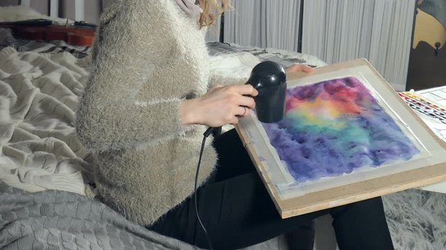 Adult women paint with colored watercolor paints and dry with a hair dryer in an art school