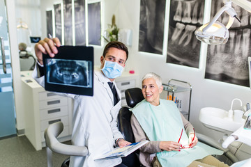 Handsome and attractive male dentist looking at dental x-ray together with his beautiful senior...