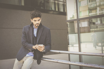Serious businessman next to building typing on mobile phone/ Space for copy.