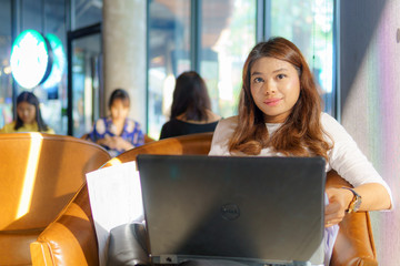 beautiful asian young business woman sitting near transparent window and business document with laptop for her project and online marketing plan at cafe . business success concept.