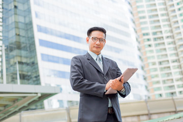 Young Asia businessman in suit with his laptop computer outdoors, modern building on the background