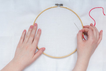 Hands of teenage girl with needle on embroidery frame on white textile background canveplian top view flat lay 