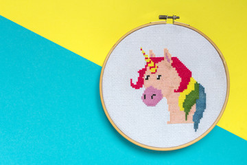 Embroidery of a unicorn on a yellow blue background with a cross in a frame, a trend of 2018, a concept of surrealism and fantasy in the style of pop art