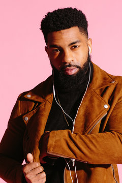 Cool man with beard reaching into his pocket, isolated on pink studio background