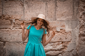 Funny young woman in hat and blue dress, looking camera, smiling, on stone street background