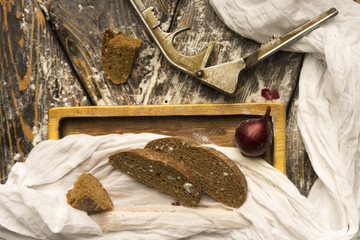 Conceptual still life of pieces of bread, on an ancient wooden table lying on a wooden tray at the nutcracker, a piece of cloth, wedges of cherry tomatoes, and an onion.