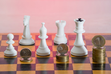 Figures of chess and a stack of coins on a chessboard. The concept of financial growth, success and victories. Strategic investment with money.