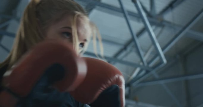 Close view from below of focused athletic woman in boxing gloves working out on technique while training with coach on ring.