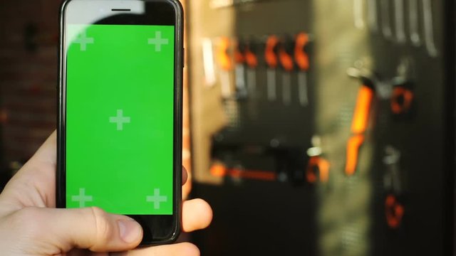 close up view of man hand using smart phone wirh empty green screen and tools shop on background pointing finger touchscreen chroma-key mock-up commercial building business application notification