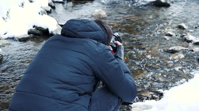 Photographer taking pictures of winter river in mountain. Travel and photography