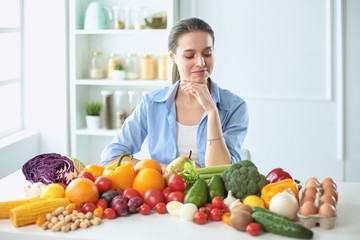 happy young housewife sitting in the kitchen preparing food from a pile of diverse fresh organic fruits and vegetables