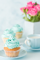 Blue pastel vertical banner with decorated cupcakes, cup of coffe with milk and bouquet of pink roses.