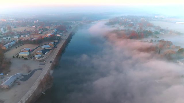 Aerial view of tranquil foggy river through small town USA at sunrise.
