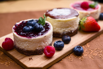 Three mini cheesecakes, one with blueberry sauce and berries decoration on brown cloth and wooden pad