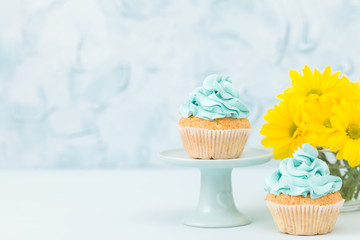 Cupcake with yellow cream decoration on vintage stand and bouquet of yellow chrysanthemum in glasses vase.