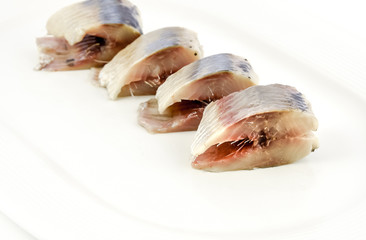 Slices of salted herring on the plate on white background.
