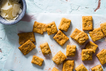 Close-up of homemade cheesy turmeric crackers on a textured blue paster surface with copper accents...