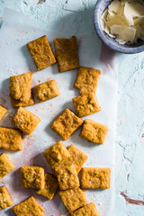 Close-up of homemade cheesy turmeric crackers on a textured blue paster surface with copper accents...