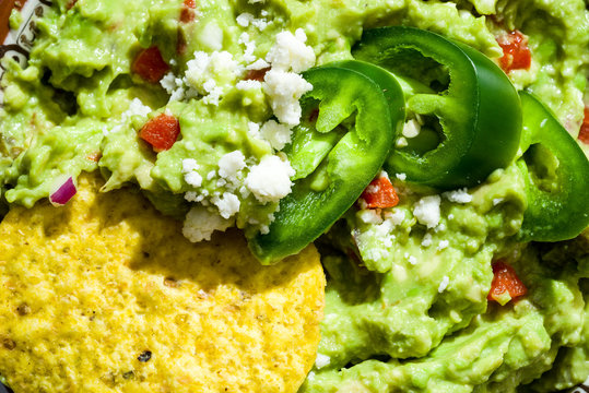 Close-up of sliced jalepenos with queso freso in pimento guacamole with round yellow corn tortilla chip.