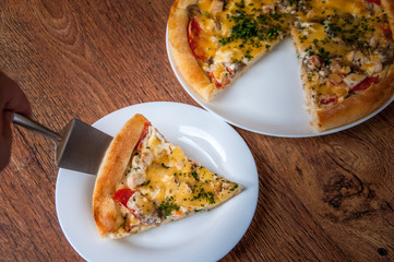 A triangular piece of pizza is taken out of it. the rest of the pizza in blur in the background.Home made pizza on white plate dish on dark oak wood table