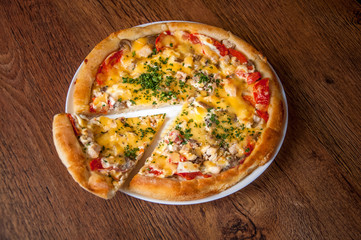 A triangular piece of pizza is separated..Home made pizza on white plate dish on dark oak wood table
