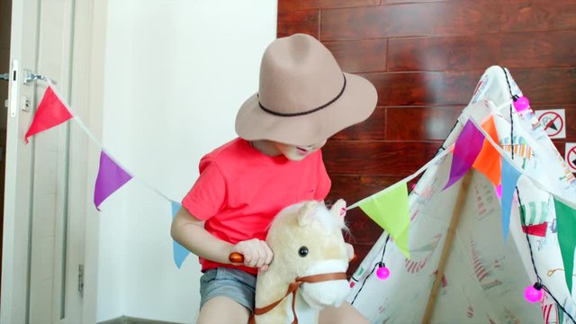 Little boy is riding a toy horse in the cowboy hat