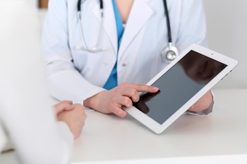  Closeup of a doctor and  patient  sitting at the desk. Physician pointing into tablet pc. Medicine and health care concept