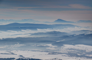 Elevated view of sunny winter scenery with blue mountain ridges, misty valleys and cone shaped Velky Choc peak, Orava and Liptov regions Oravska Magura Chocske vrchy Nizke Tatry ranges Slovakia Europe