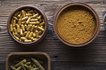 Curcuma capsules, turmeric roots and powder in bowls. Anti cancer medicine. Wooden table. Top view shot.