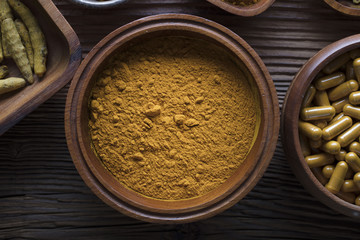 Curcuma capsules, turmeric roots and powder in bowls. Anti cancer medicine. Wooden table. Top view shot.