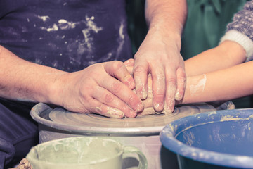 Potter's hands guiding child's hands to help him to work with the pottery wheel. Little girl learns to sculpt from clay