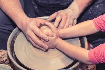 Potter's hands guiding child's hands to help him to work with the pottery wheel. Little girl learns to sculpt from clay