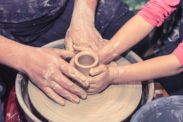 Potter's hands guiding child's hands to help him to work with the pottery wheel. Little girl learns to sculpt from clay