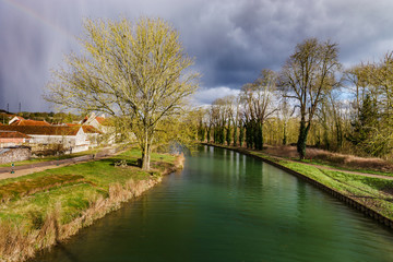 Fototapeta na wymiar Green water of canal and blue sky, springtime in countryside
